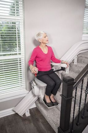 An elderly woman is sitting on a stair lift.