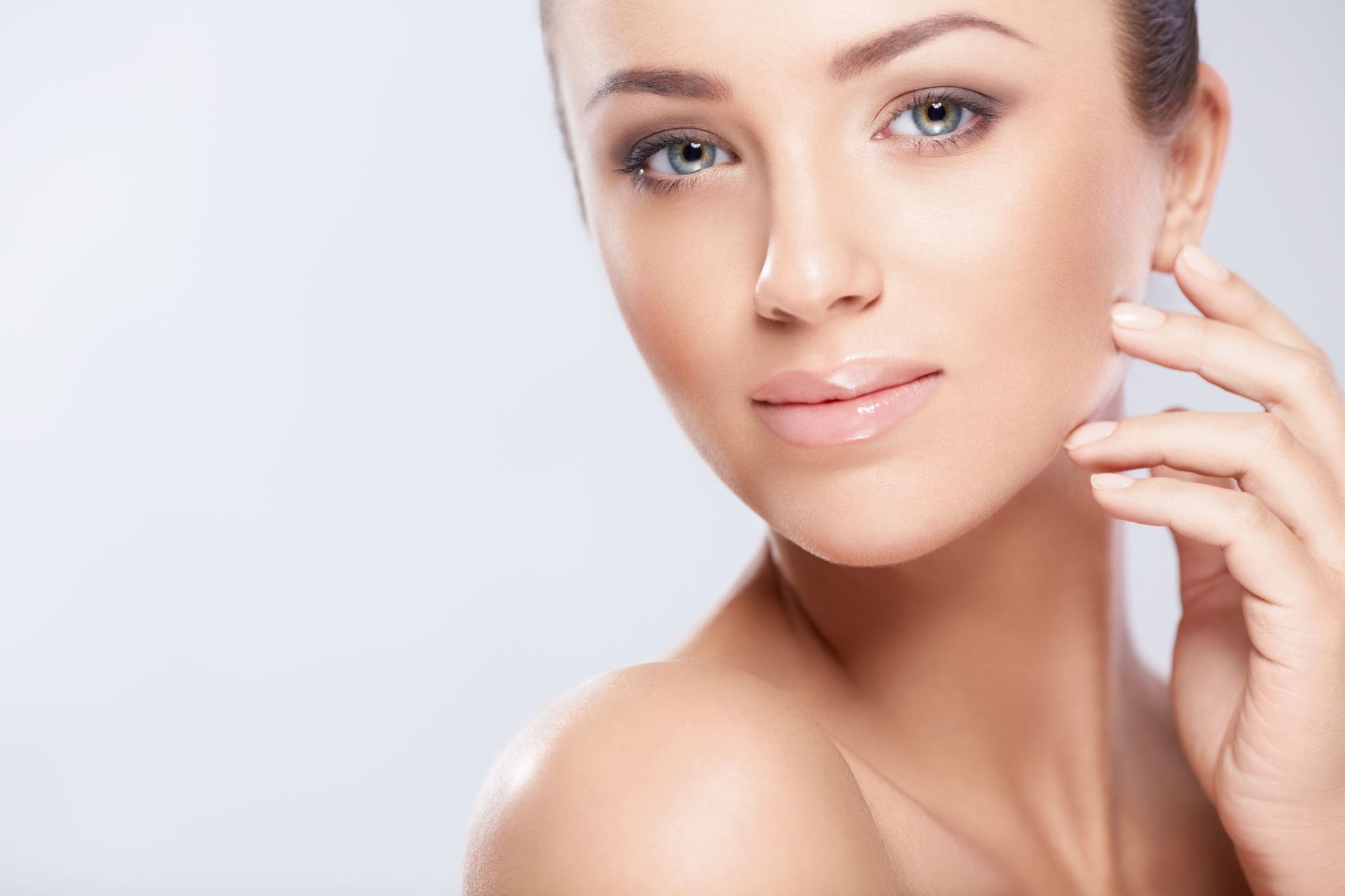 Woman with brown hair and eye makeup, touching cheek, looking forward.