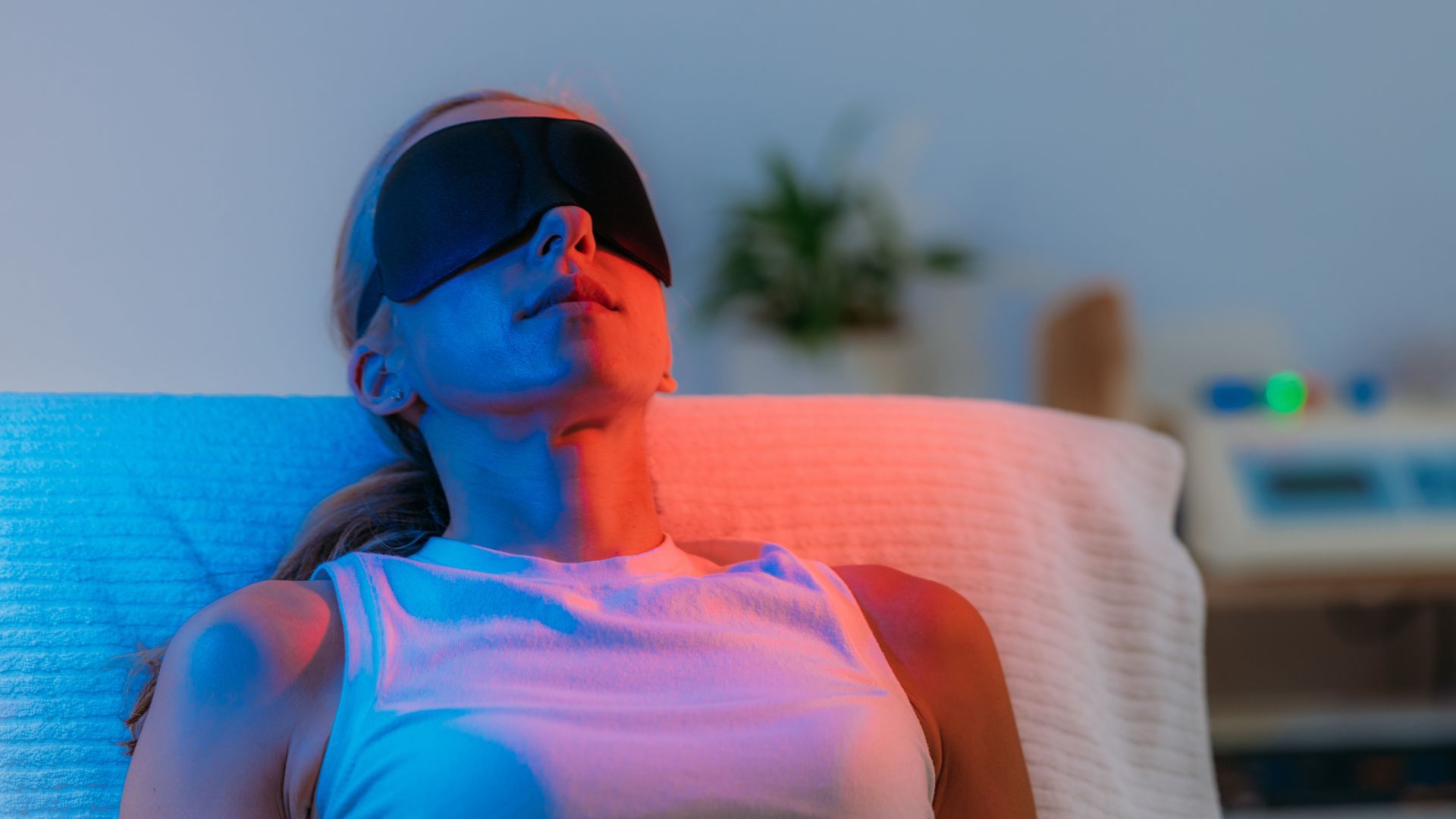 Person reclining with eye mask under red and blue light therapy in a clinical setting.
