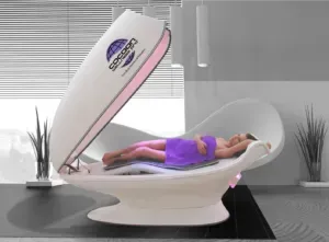 Woman lies in a white Cocoon Wellness Pod, lid open, purple towel, room with plants.