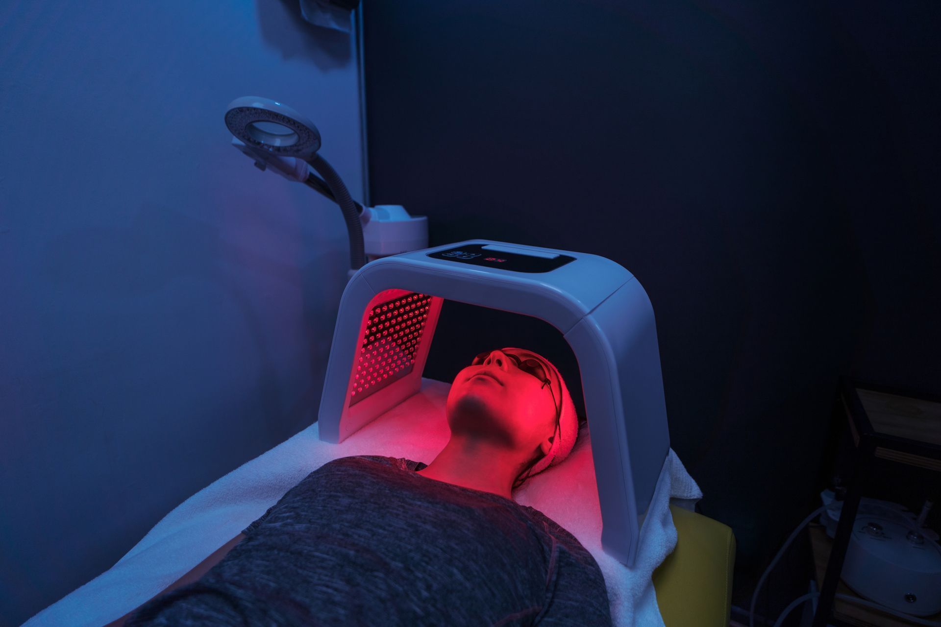 Person receiving red light therapy in a spa-like setting; head under the light, eyes closed.