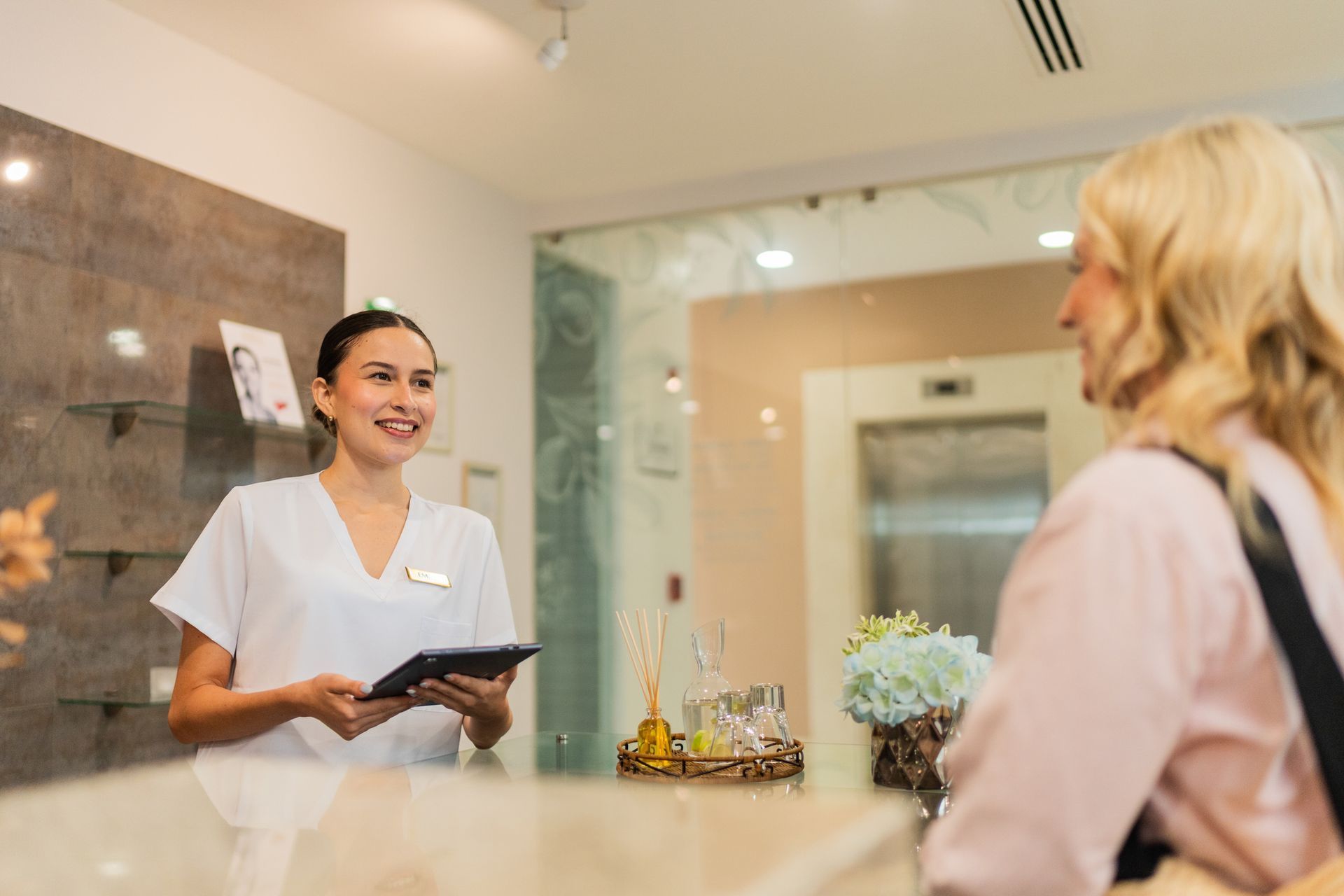 Receptionist in white uniform smiles at a customer at a clinic reception desk.