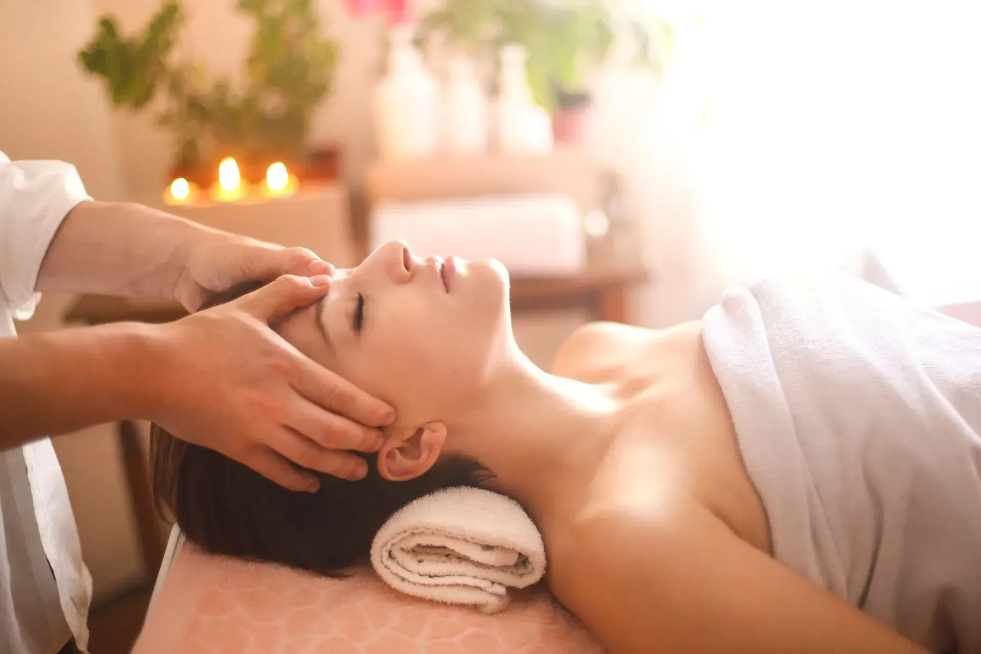 Woman receiving a head massage on a spa bed, lit by sunlight.