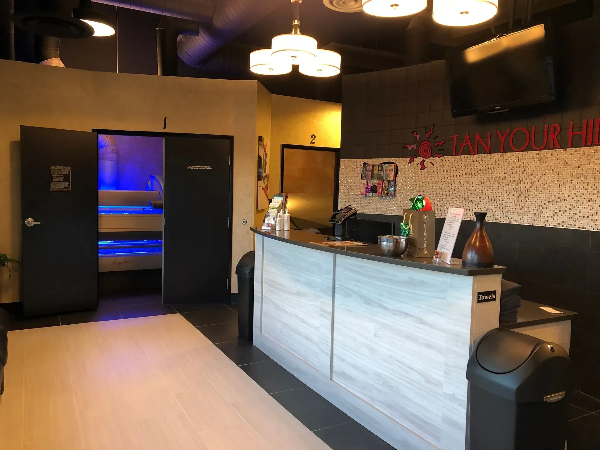Reception area of a spa. A counter, door to a room with blue light, and dark walls.