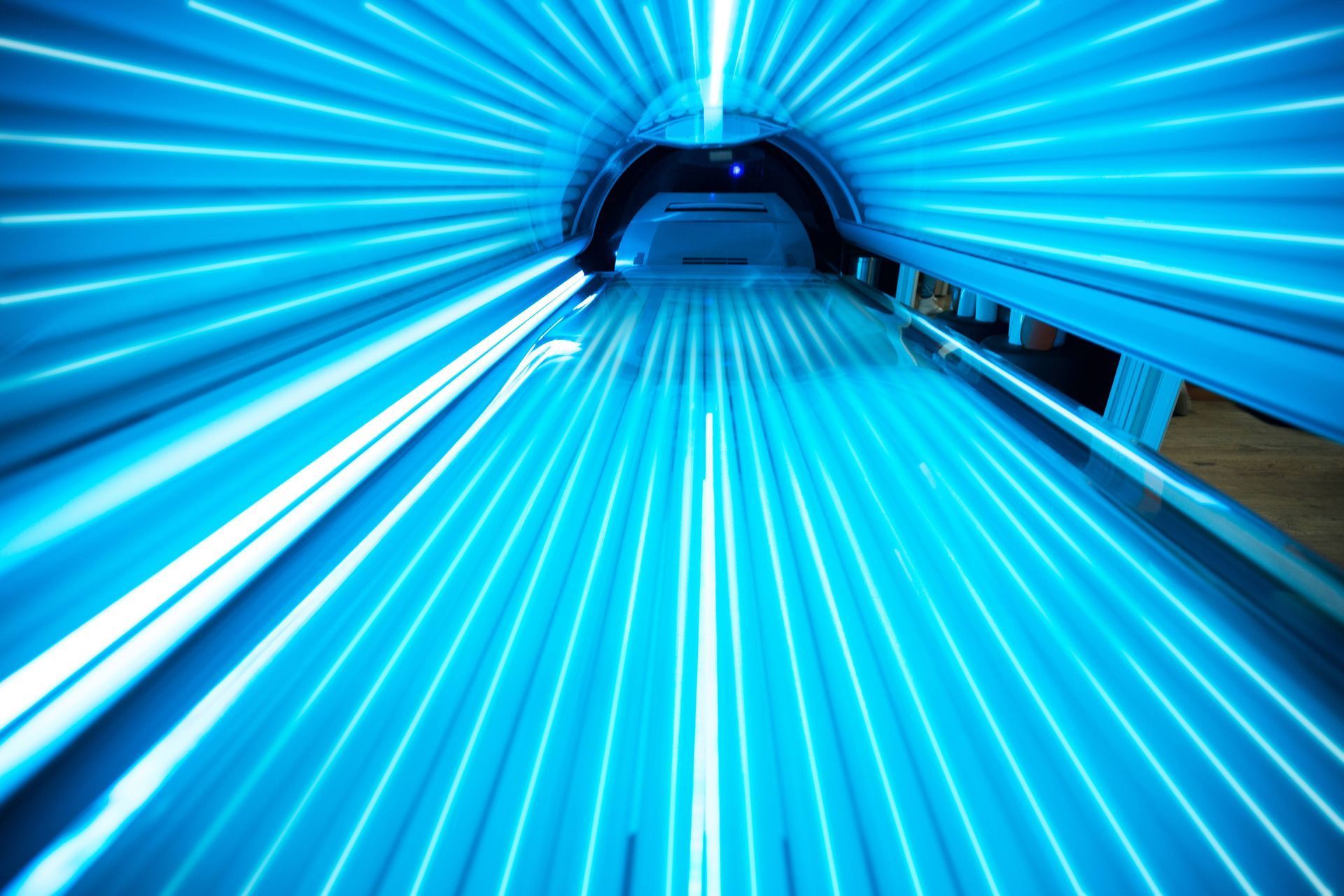 Inside a lit tanning bed, bright blue light beams illuminate.