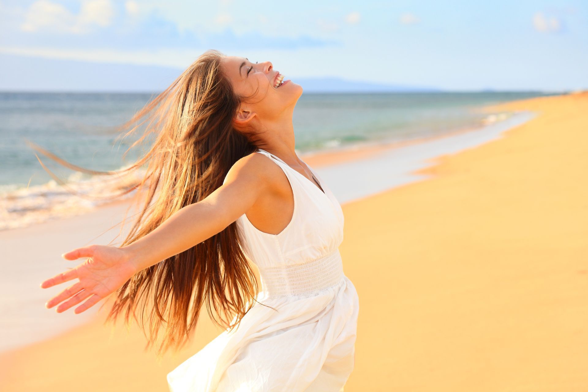 Woman on beach, arms outstretched, smiling, enjoying the sunlight and ocean breeze.