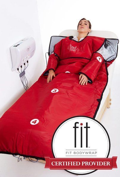 Woman in a red body wrap on a massage table, using an electronic device on the wall.
