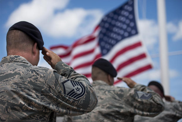 Air Force personnel saluting in front of the American flag.