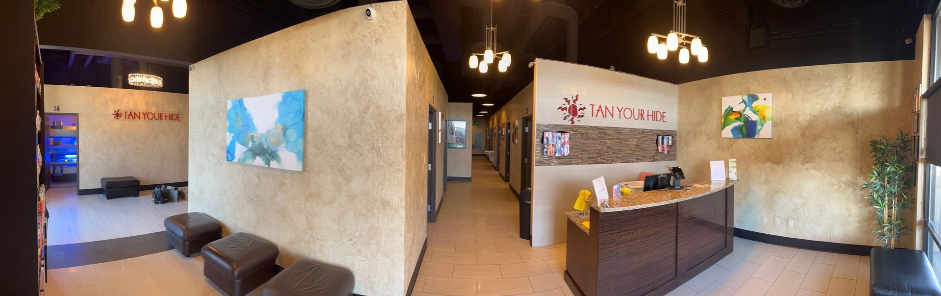 Interior of a spa. Walls are textured tan with art. There's a reception desk, a waiting area, and a hallway with treatment rooms.