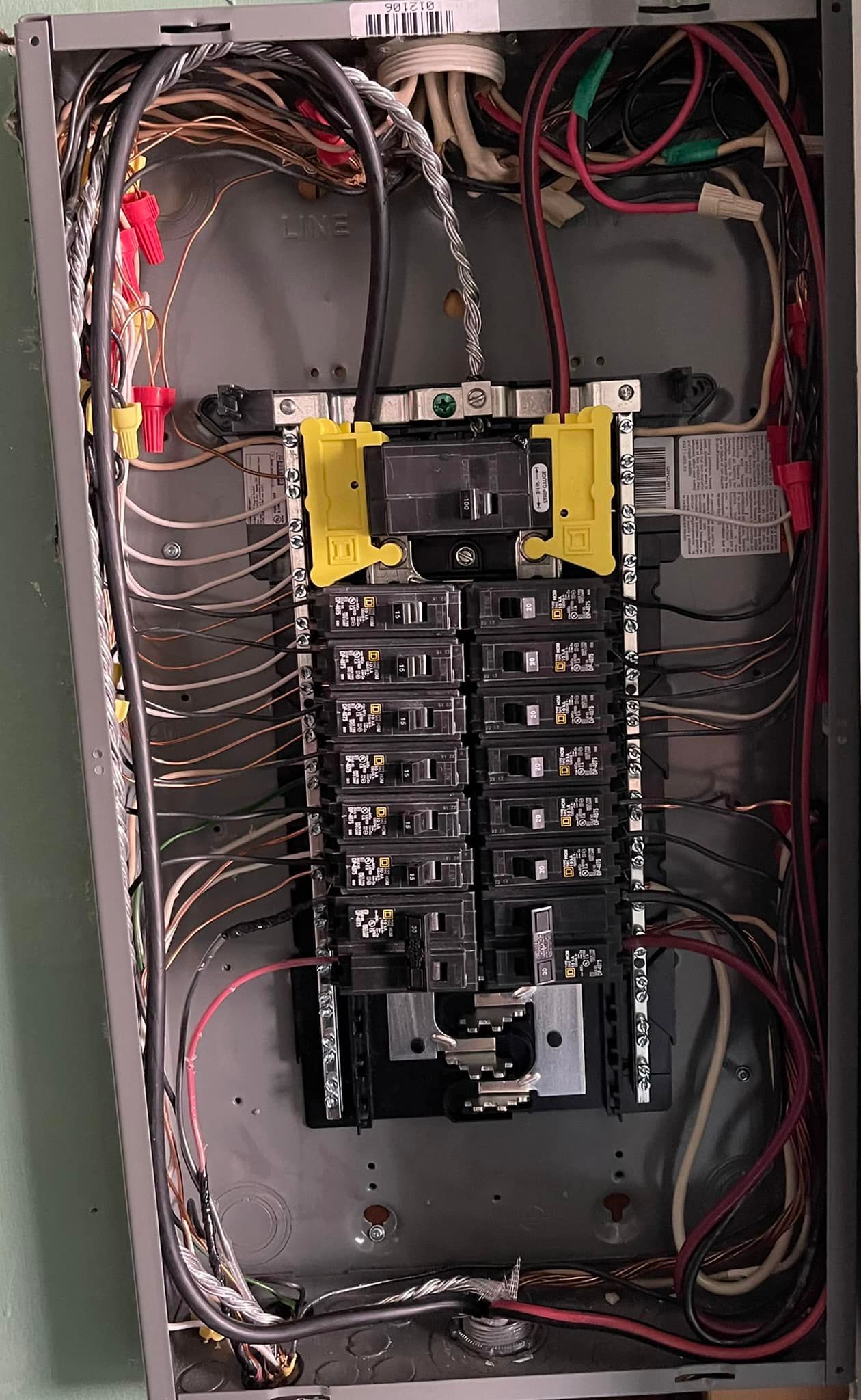 Open residential electrical circuit breaker panel with numerous wired connections and a central main breaker switch.
