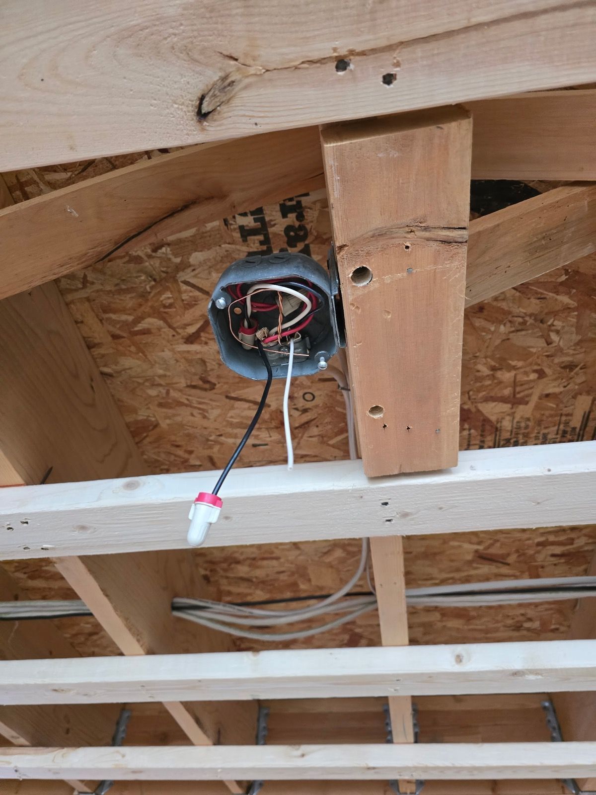 An electrical junction box mounted to wood framing, with exposed black and white wires extending from the opening.