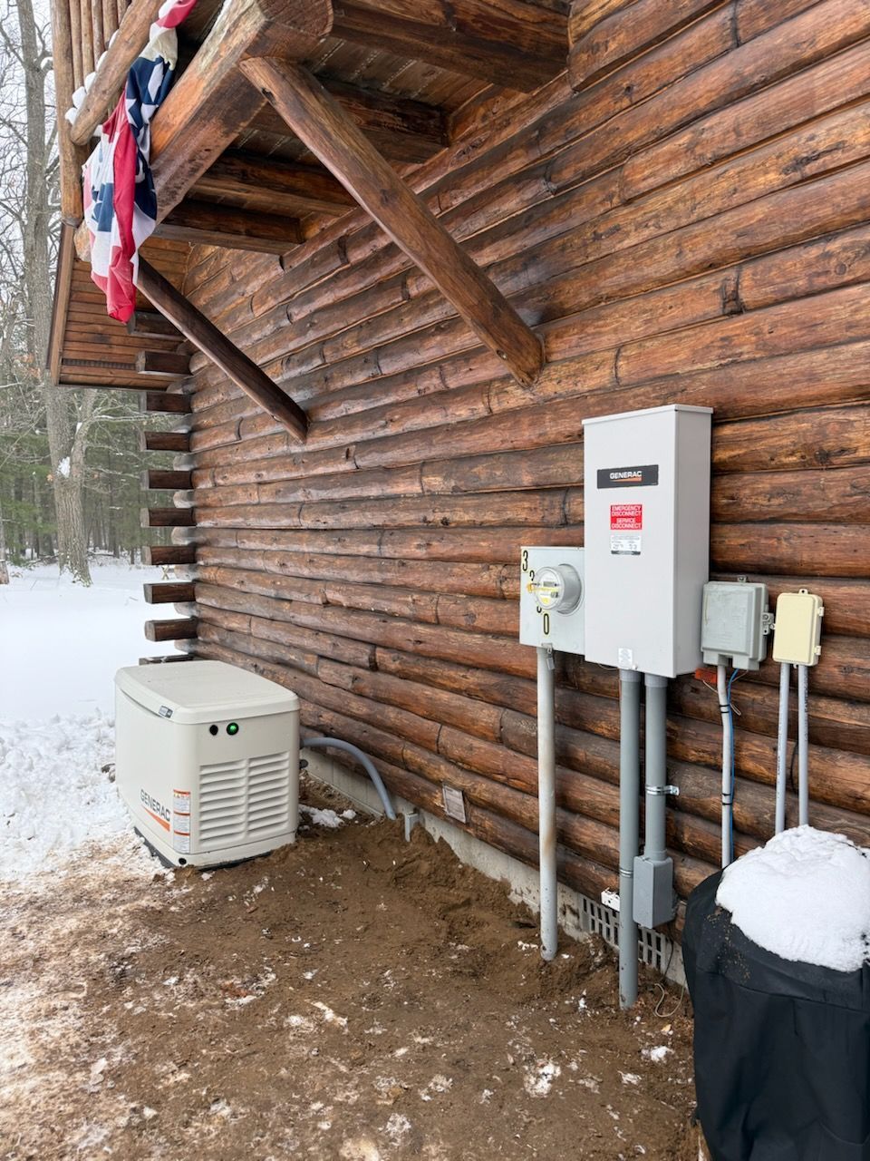 A Generac home standby generator and electrical service equipment mounted on the exterior wall of a log cabin in winter.