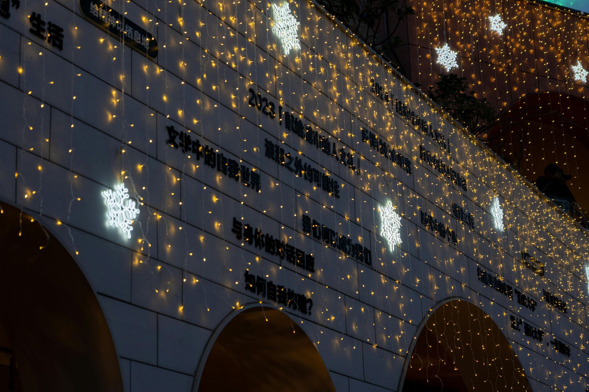 A brick wall adorned with bright white star-shaped lights and strings of golden fairy lights at night.