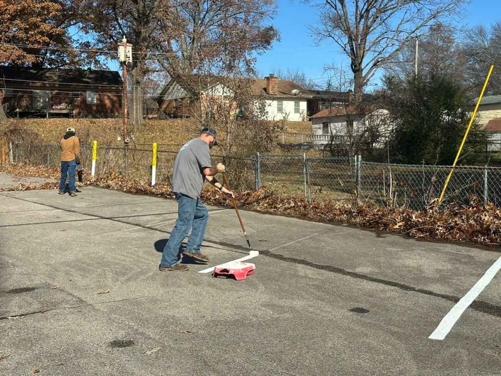 A man is sweeping a parking lot with a broom.