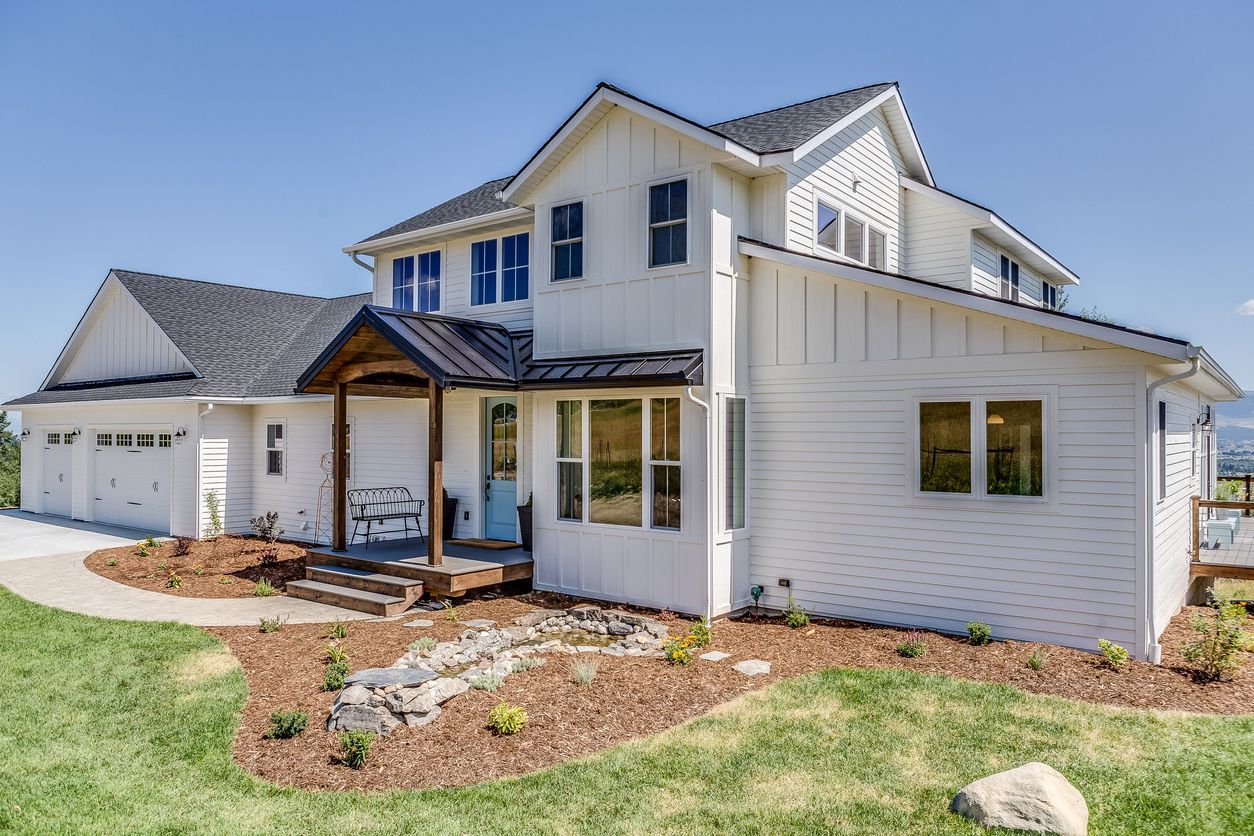 A two-story, white farmhouse-style home with a dark shingled roof, a blue front door, and a three-car garage.