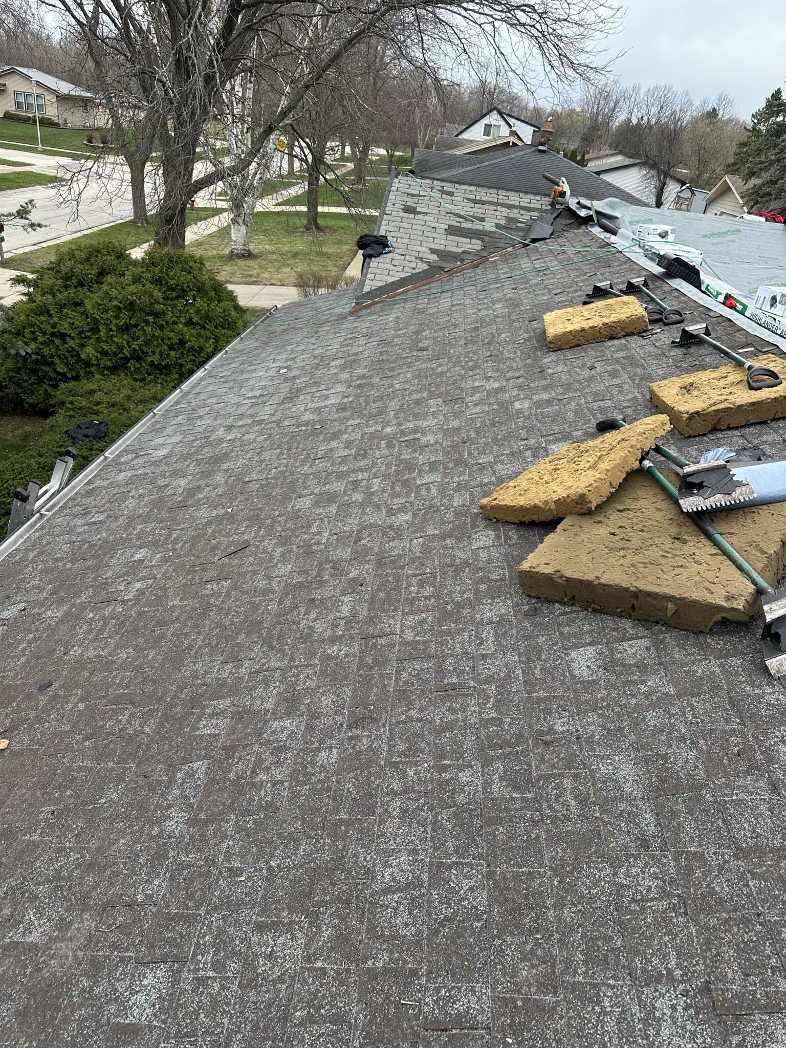 A sloped roof under construction with removed asphalt shingles, scattered debris, and yellow foam insulation boards.