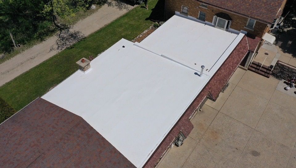 An aerial view of a house with a large, white flat roof installed next to a section of existing shingled roofing.