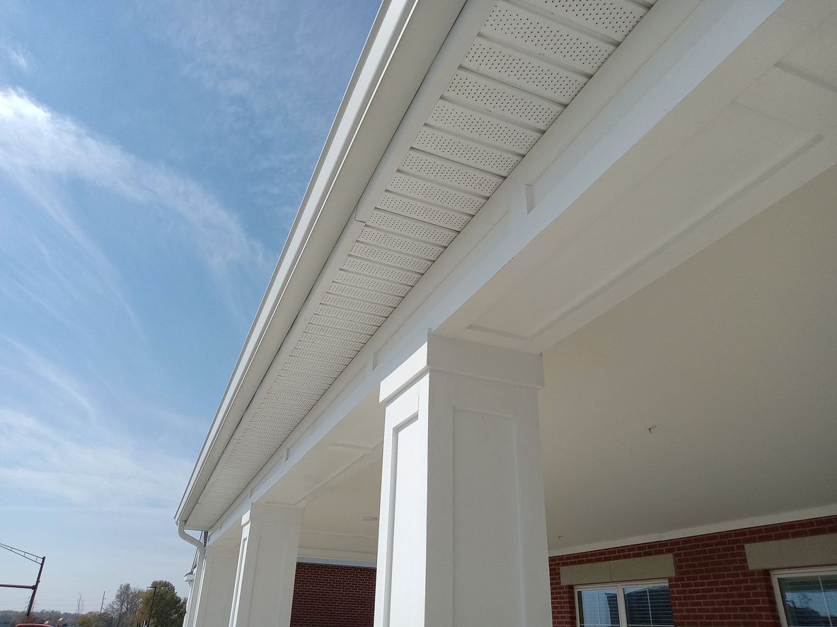 Low-angle view of white porch columns and a decorative vented soffit under a blue sky.