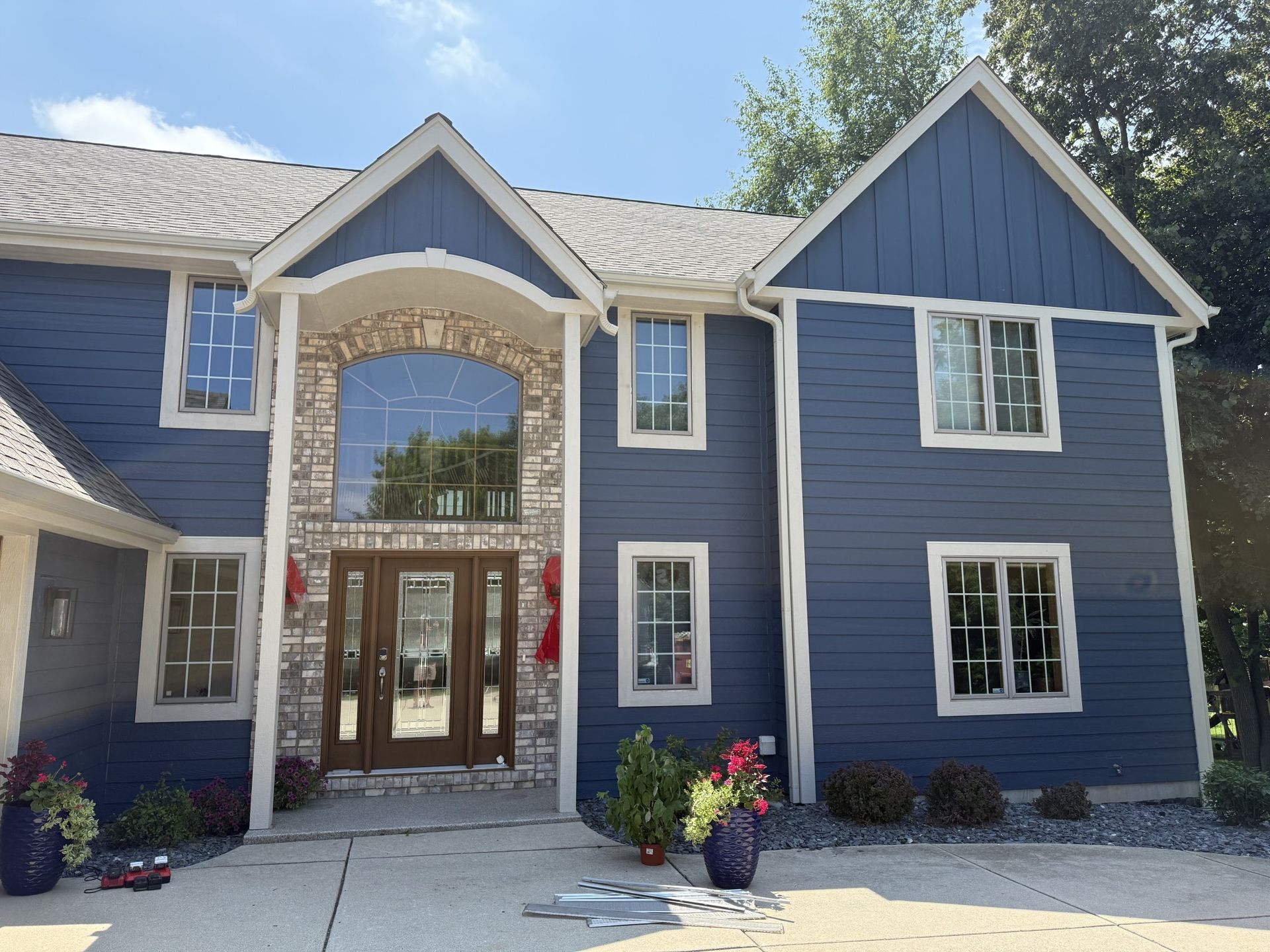 Two-story suburban house with blue horizontal siding, a stone-accented entryway, a large arched window, and potted plants.