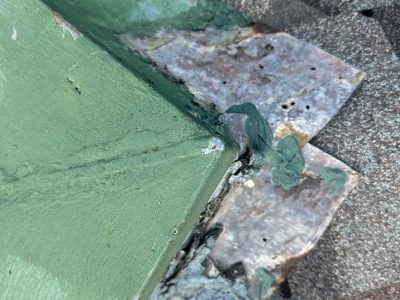 Close-up of a weathered, green-painted roof flashing corner with visible metal oxidation and sealant residue.