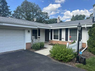 A light-gray suburban ranch home with a white garage, dark shutters, and a small white picket fence near the entrance.
