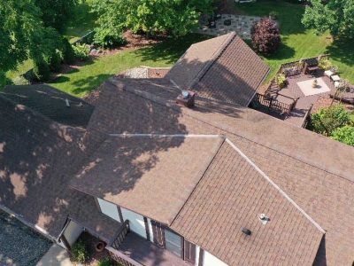 Aerial view of a brown shingled roof on a residential home with a surrounding yard and wooden deck.