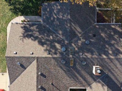 Aerial view of a complex shingled residential roof with multiple vents, skylights, and a chimney.