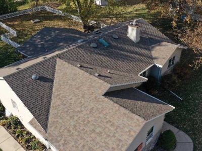 High-angle aerial view of a residential house with a shingled roof, a chimney, and skylights, surrounded by a yard.