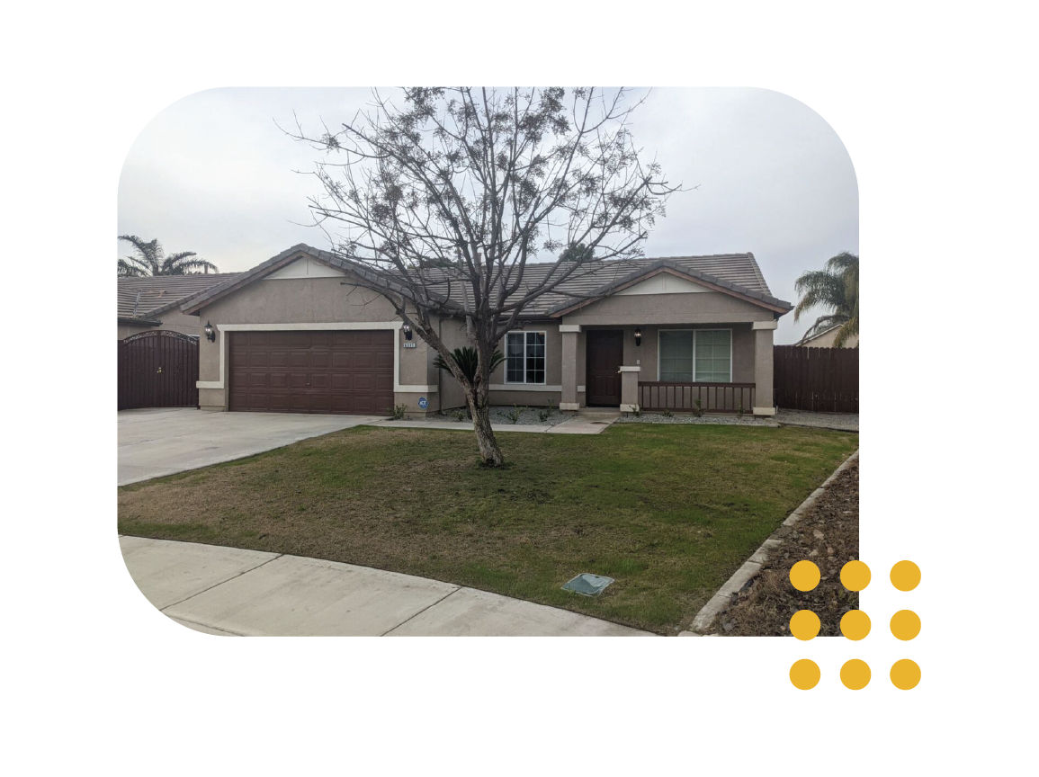 A single-story, beige suburban house with a two-car garage, a bare tree in the front yard, and a small covered porch.