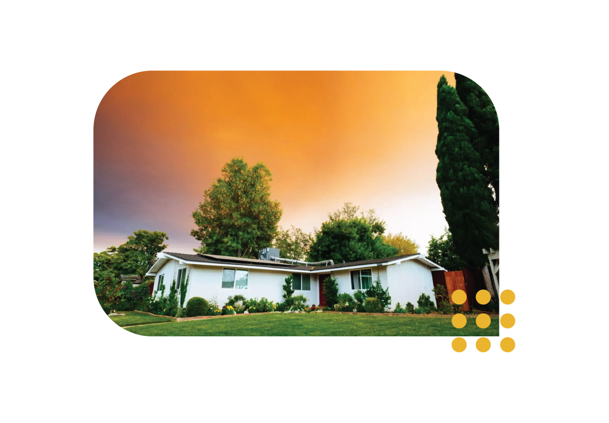 A single-story white house surrounded by trees under a dramatic, orange-hued sunset sky.