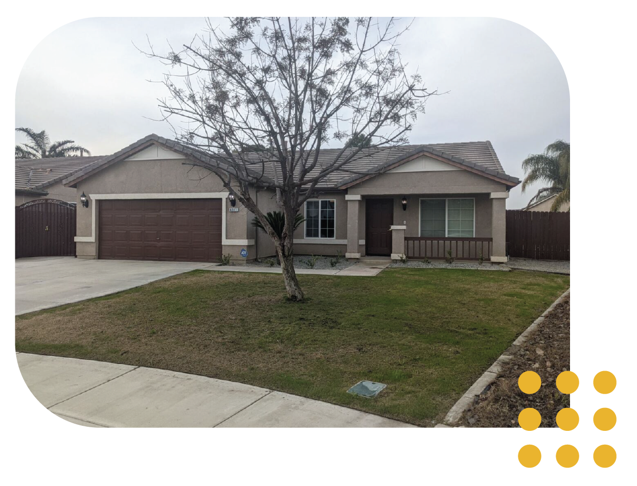 A single-story, beige suburban house with a two-car garage, a bare tree in the front yard, and a small covered porch.