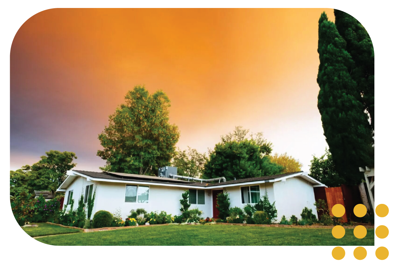 A single-story white house surrounded by trees under a dramatic, orange-hued sunset sky.