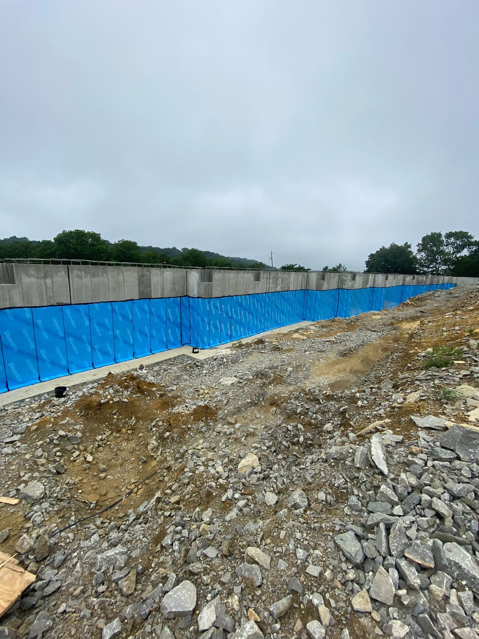 A large blue tarp is covering a concrete wall in a rocky area.