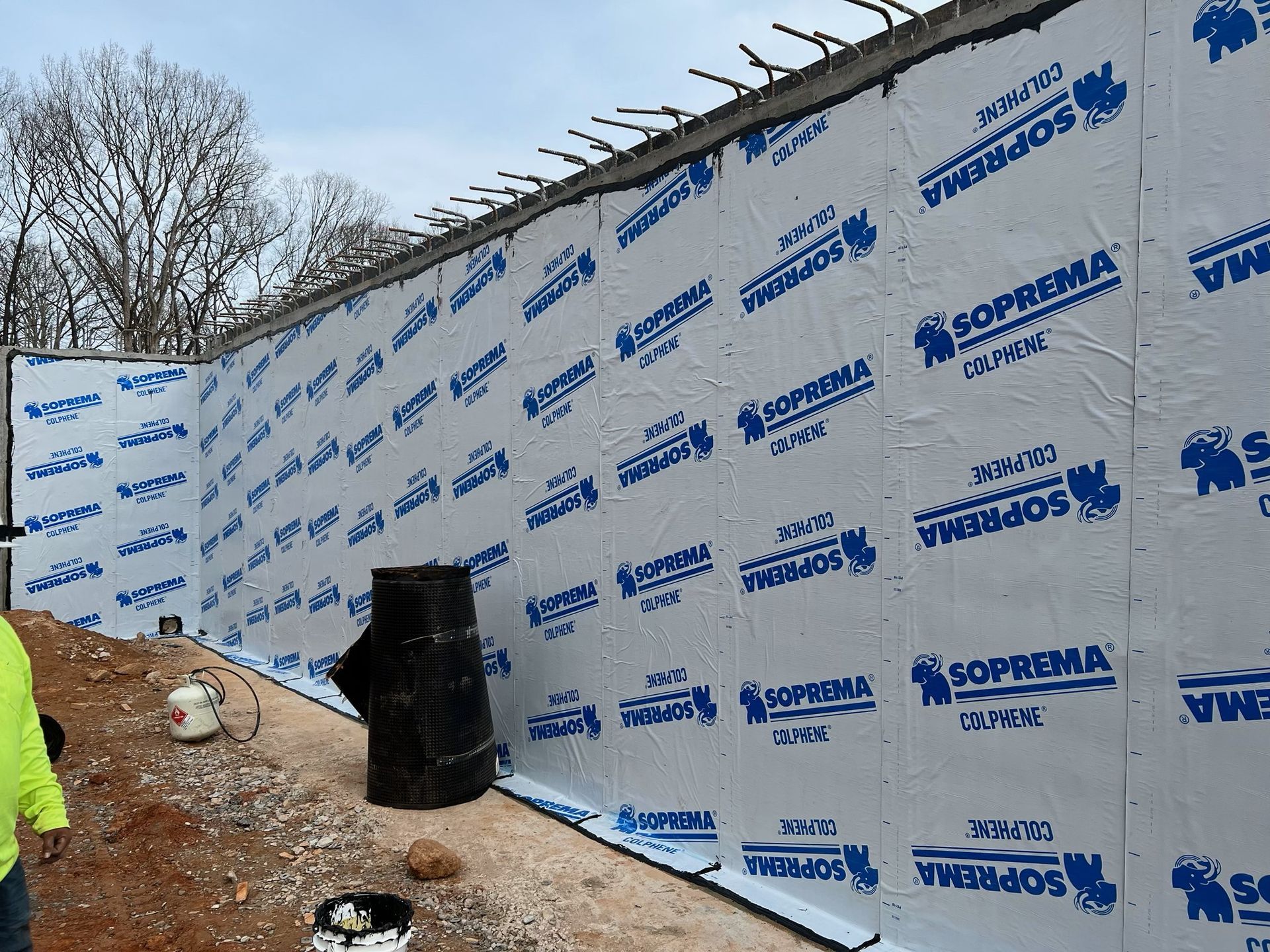 A man in a yellow vest is standing in front of a wall that says soprama on it