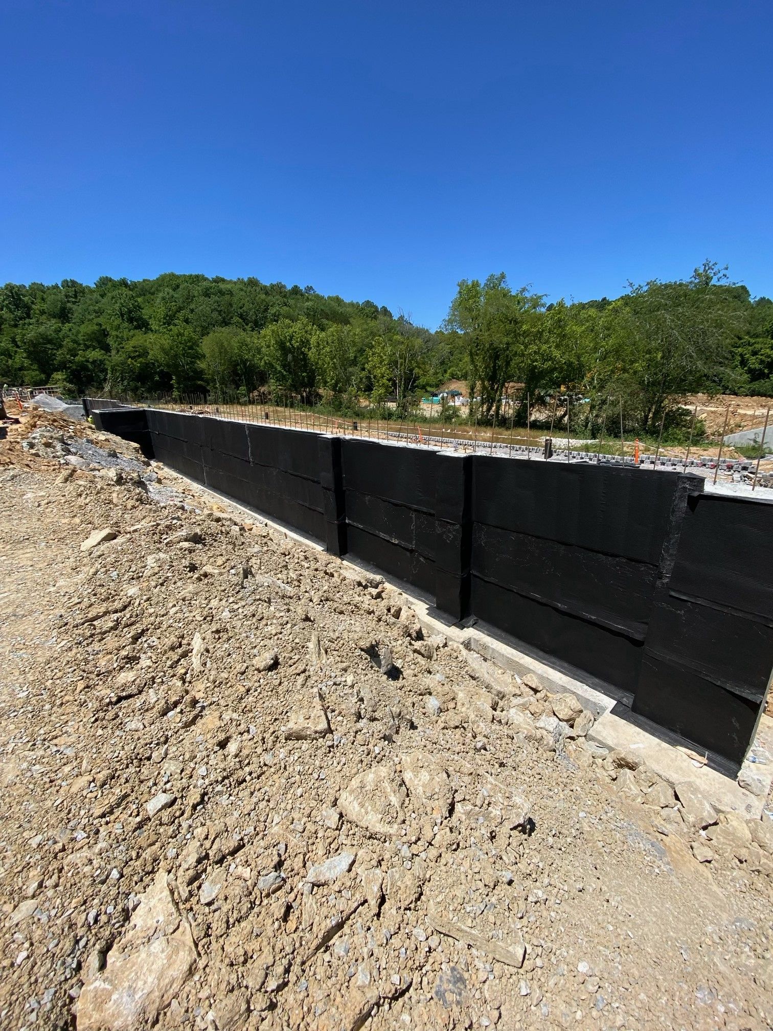A concrete wall is being built in a dirt field with trees in the background.