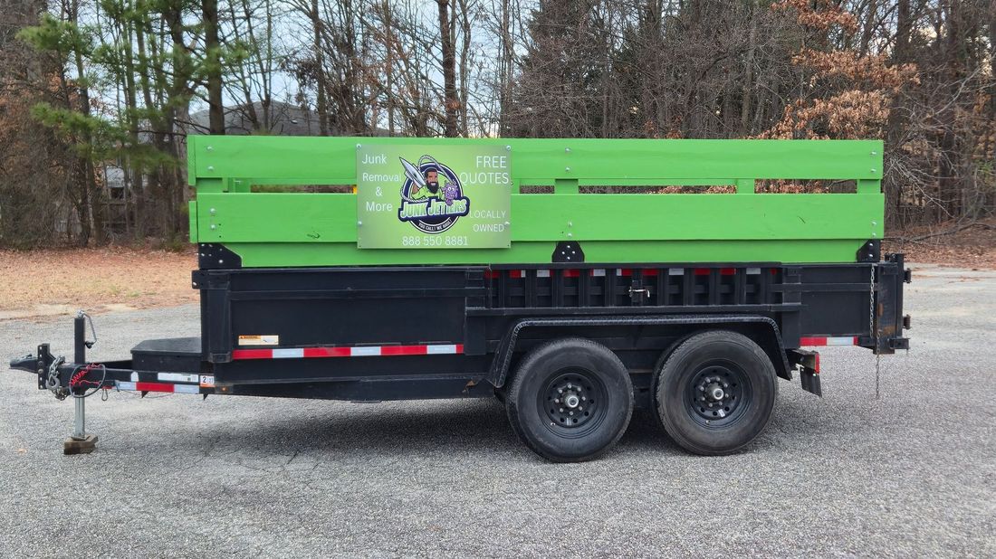 A black dump trailer with green side extensions and a promotional logo parked on a gravel lot.