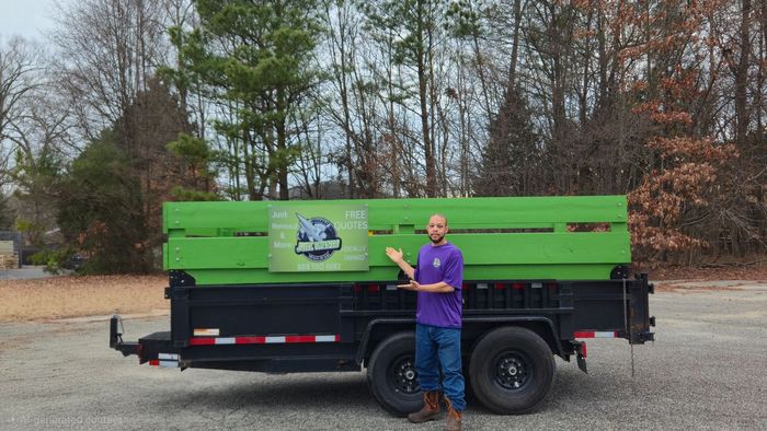 A person in a purple shirt standing beside a black trailer with a large green crate labeled