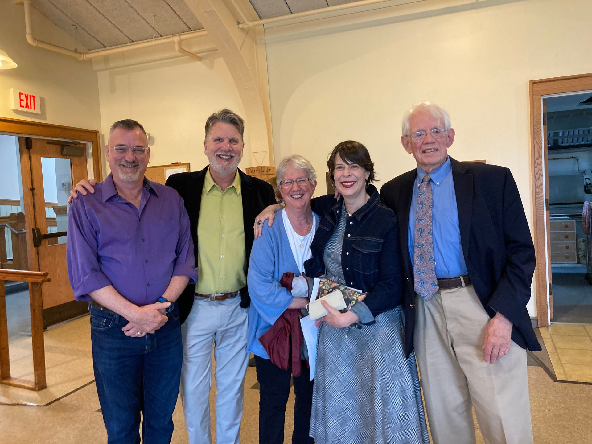 Group of five people smiling in a room with an exit and doorway.