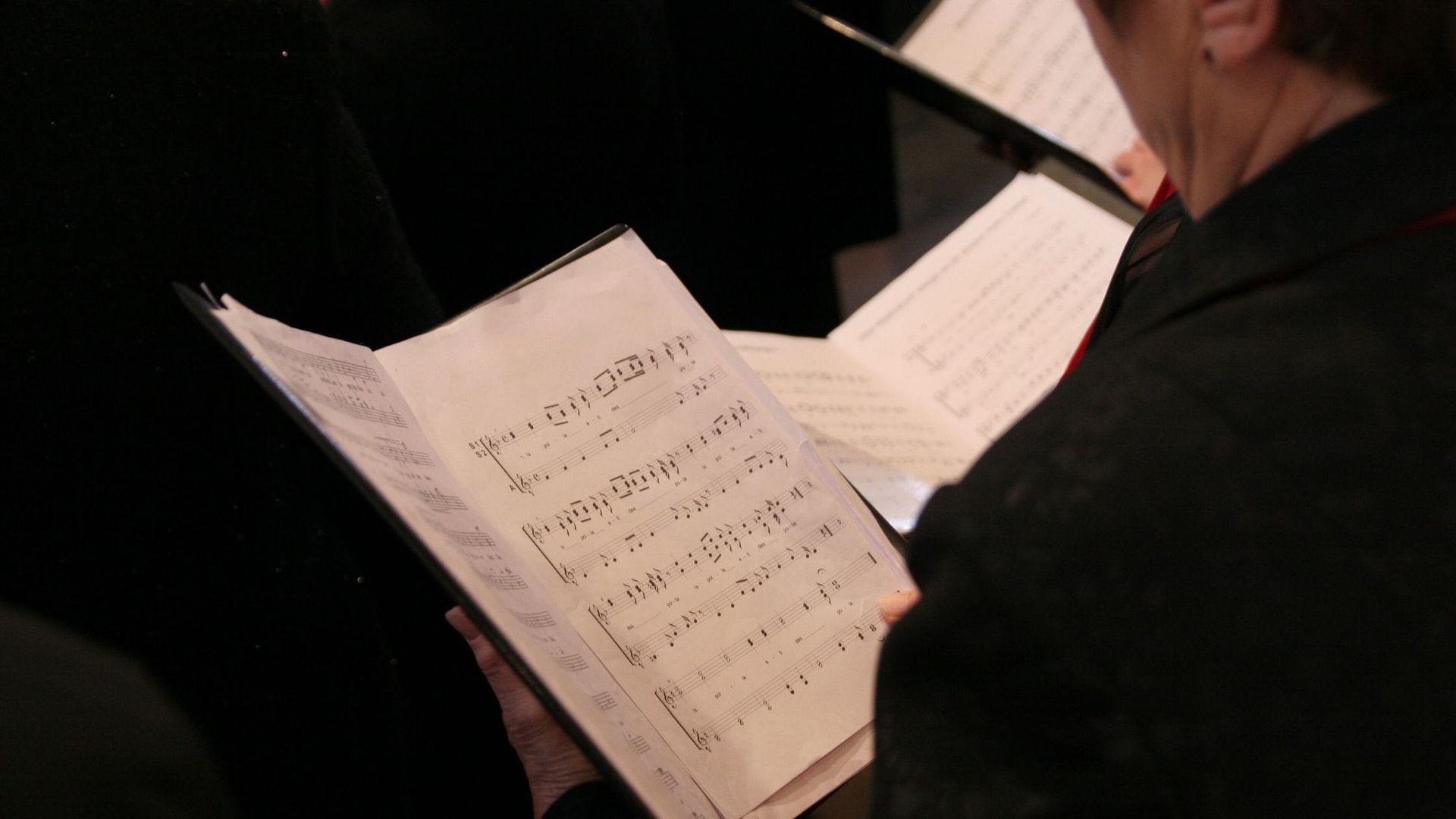 A woman is reading sheet music in a choir