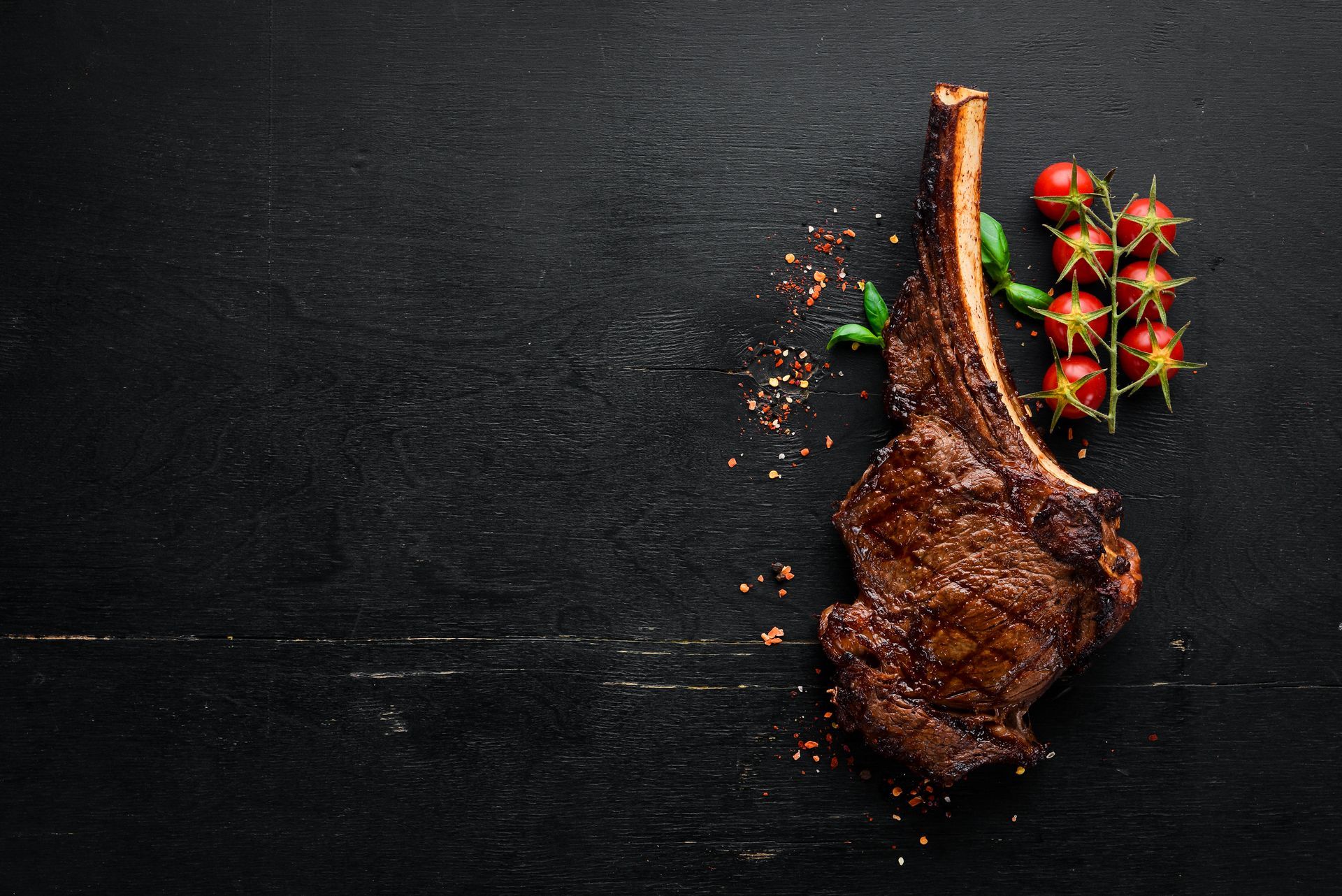 A steak on a bone with tomatoes on a black background.