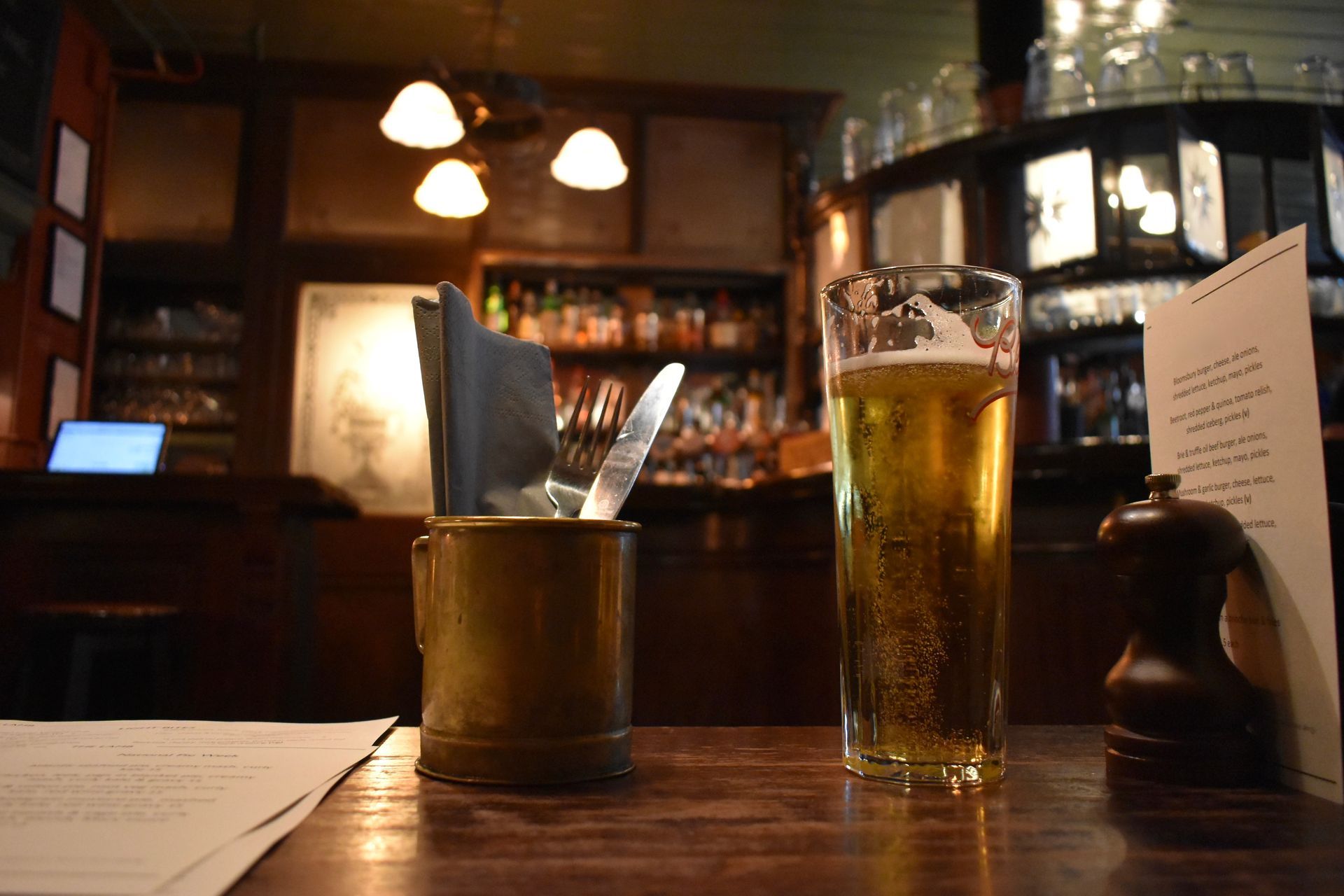 A glass of beer is sitting on a wooden table in a restaurant.