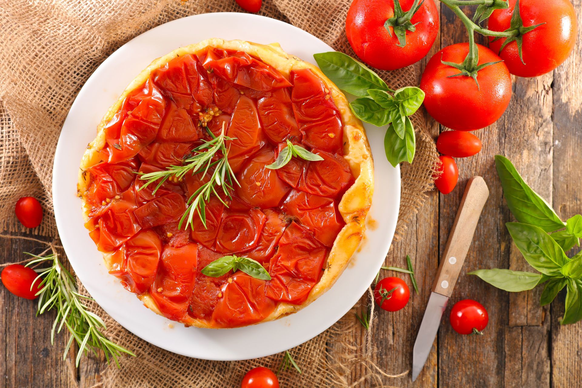 A pizza with tomatoes and basil on a white plate on a wooden table.