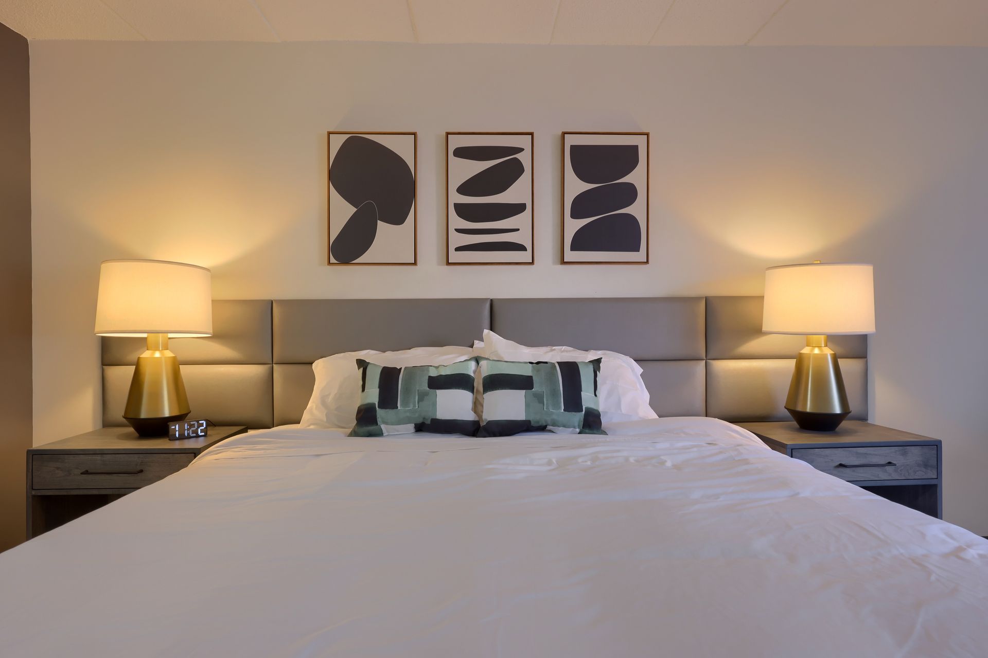 A bedroom with a bed , two lamps , and three paintings on the wall.