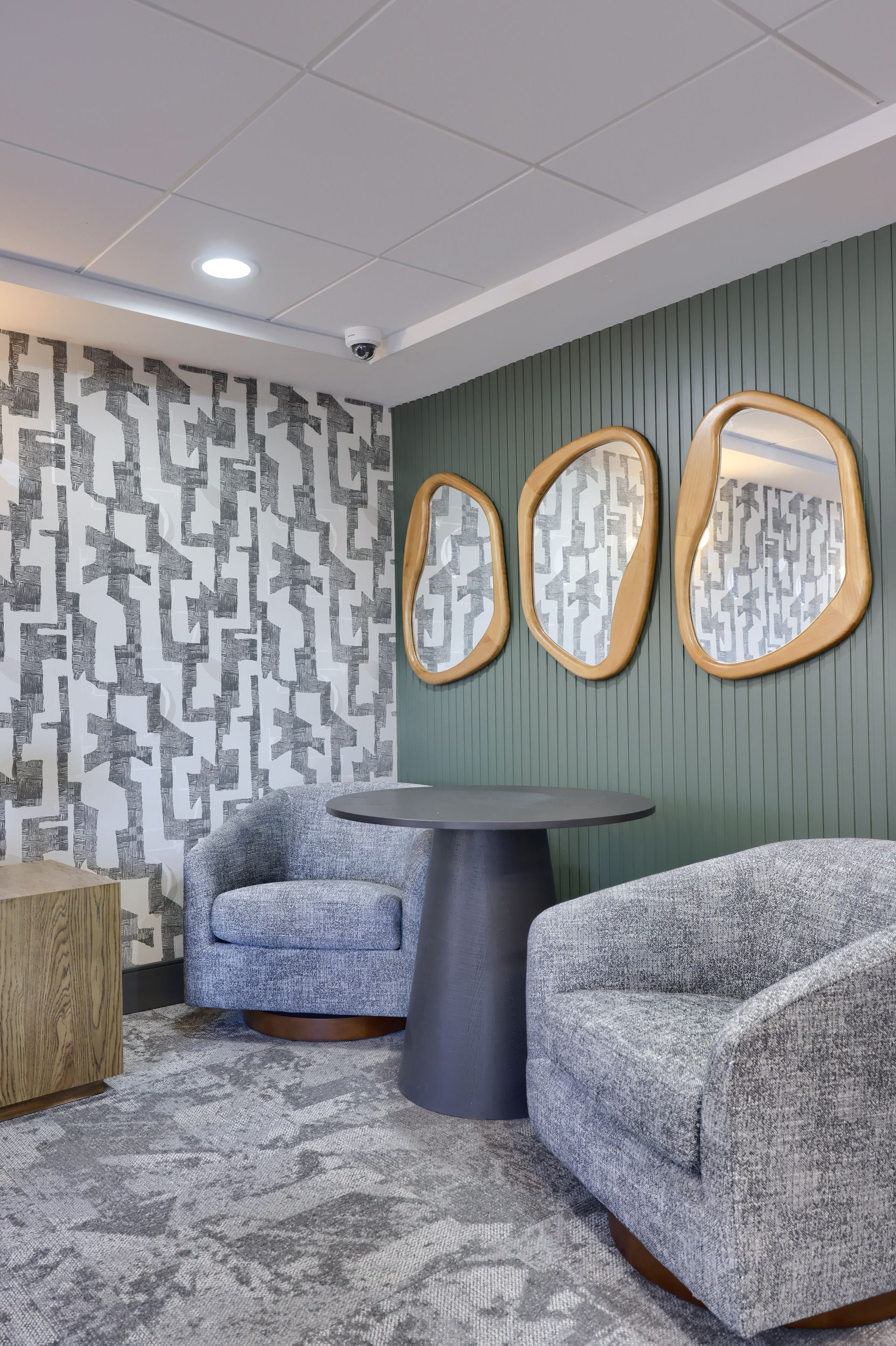 A living room with chairs , a table and mirrors on the wall.