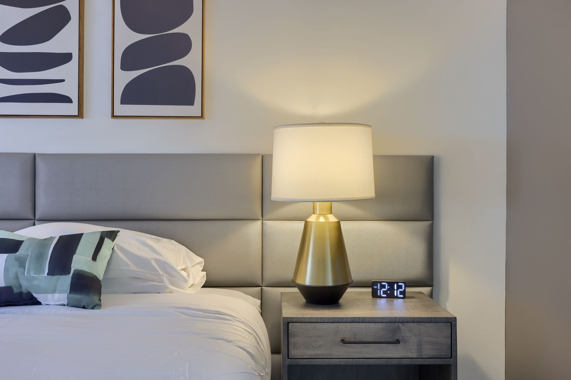 A bedroom with a bed , nightstand , lamp and clock.