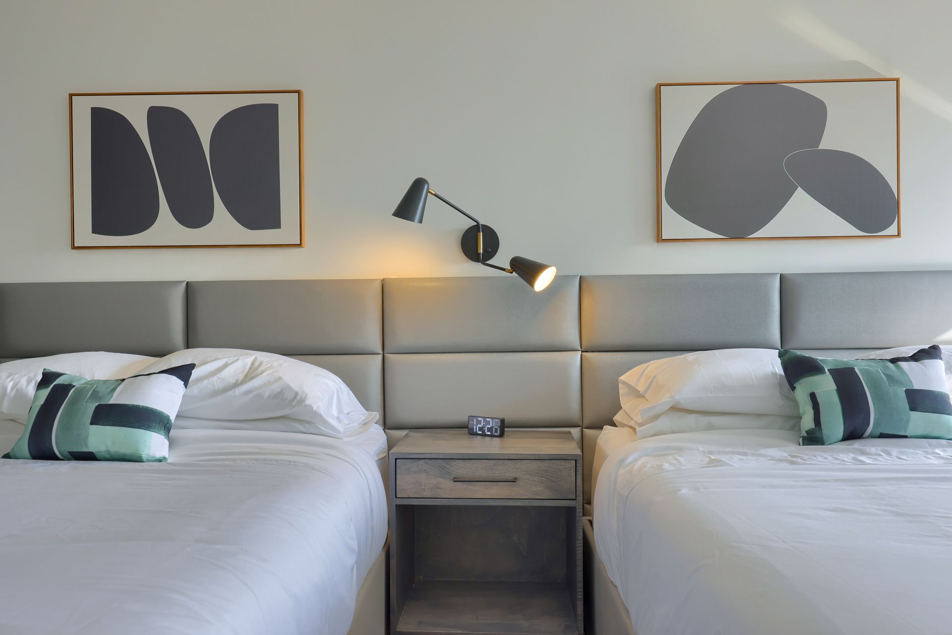A hotel room with two beds , two nightstands and two paintings on the wall.