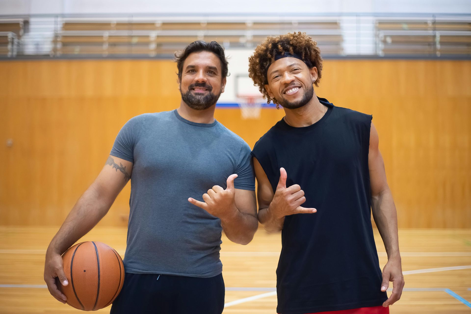 Two men are standing next to each other on a basketball court holding a basketball.