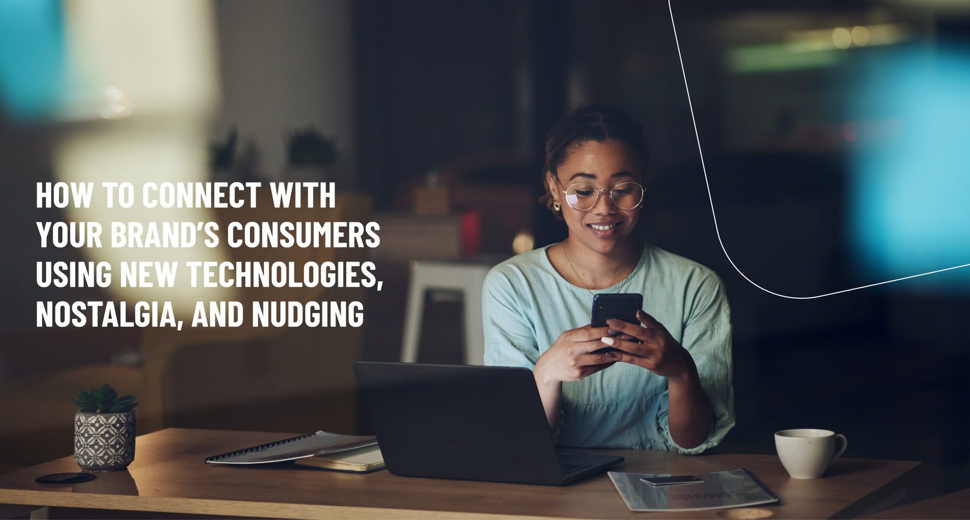 A woman sits at a desk with her laptop open whilst holding a smartphone.