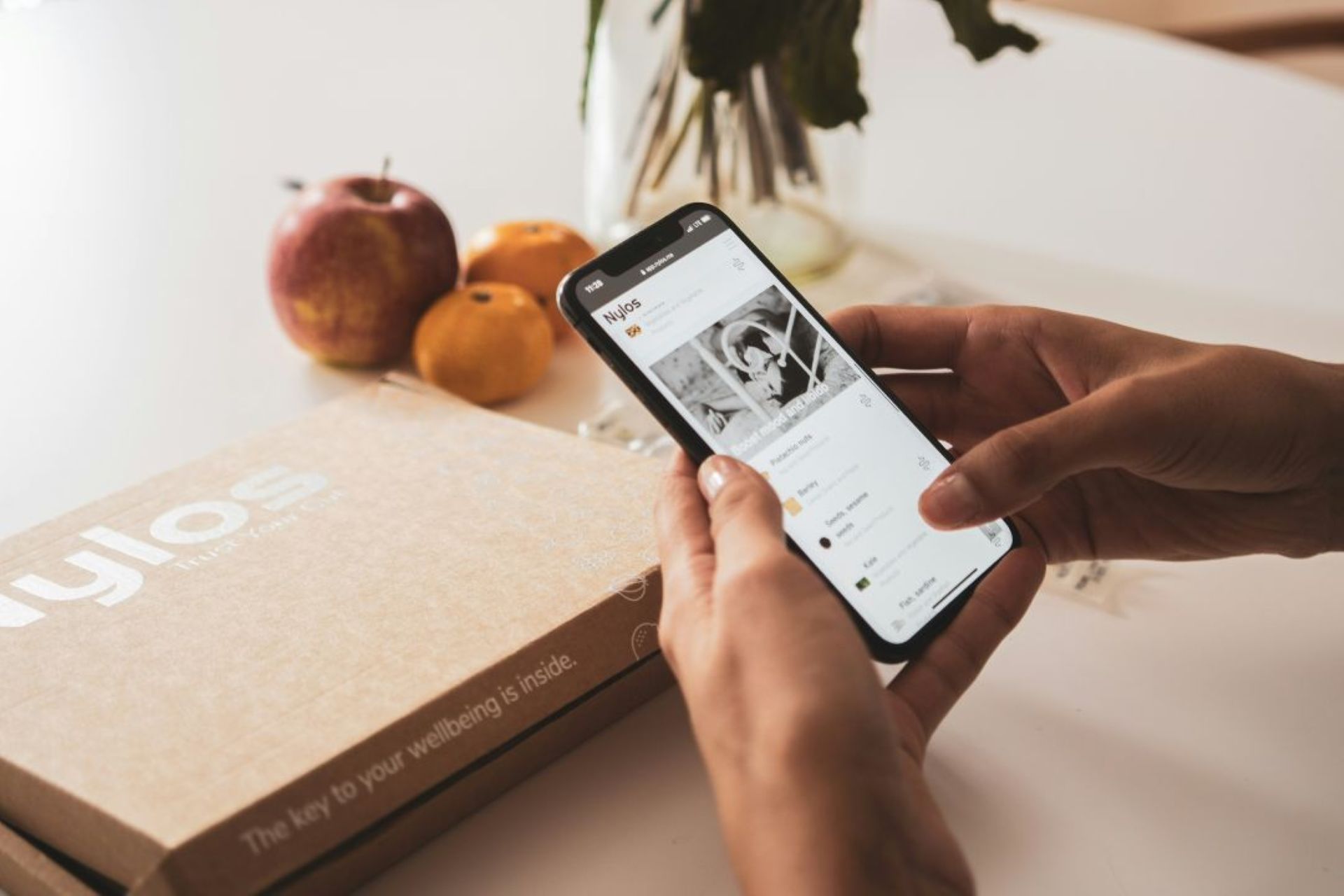 Close up of a person holding a mobile phone showing the home screen of a brand profile with a branded box nearby