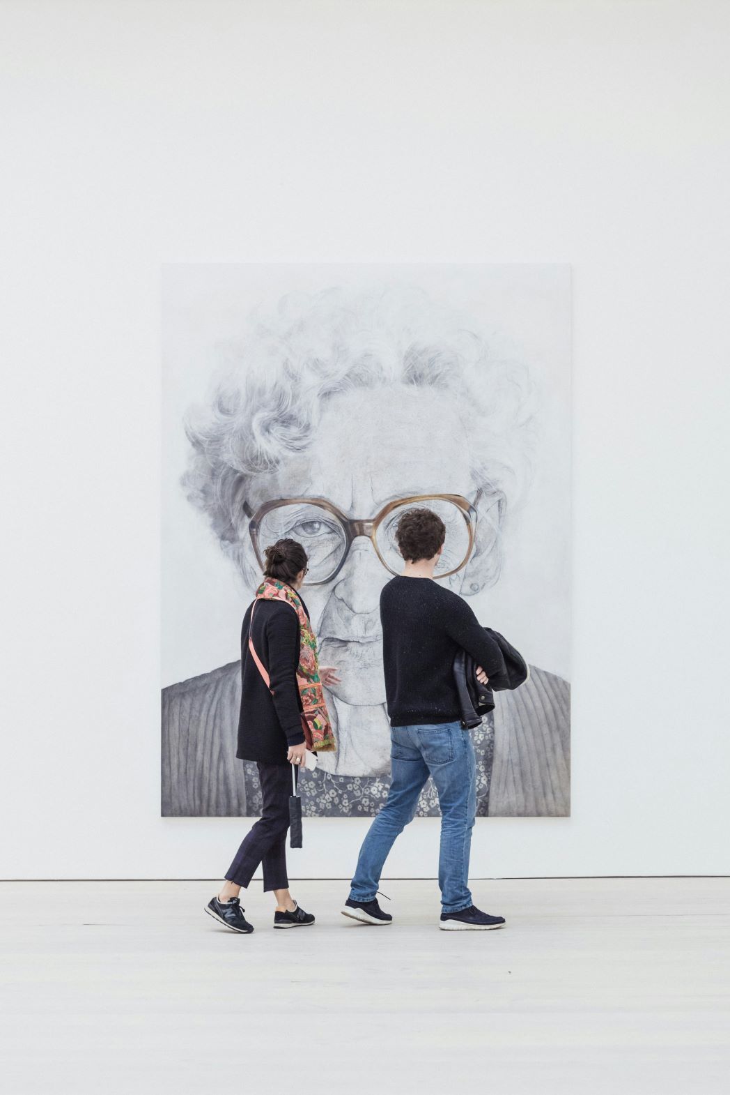 A man and a woman walk past a large piece of artwork showing an elderly lady